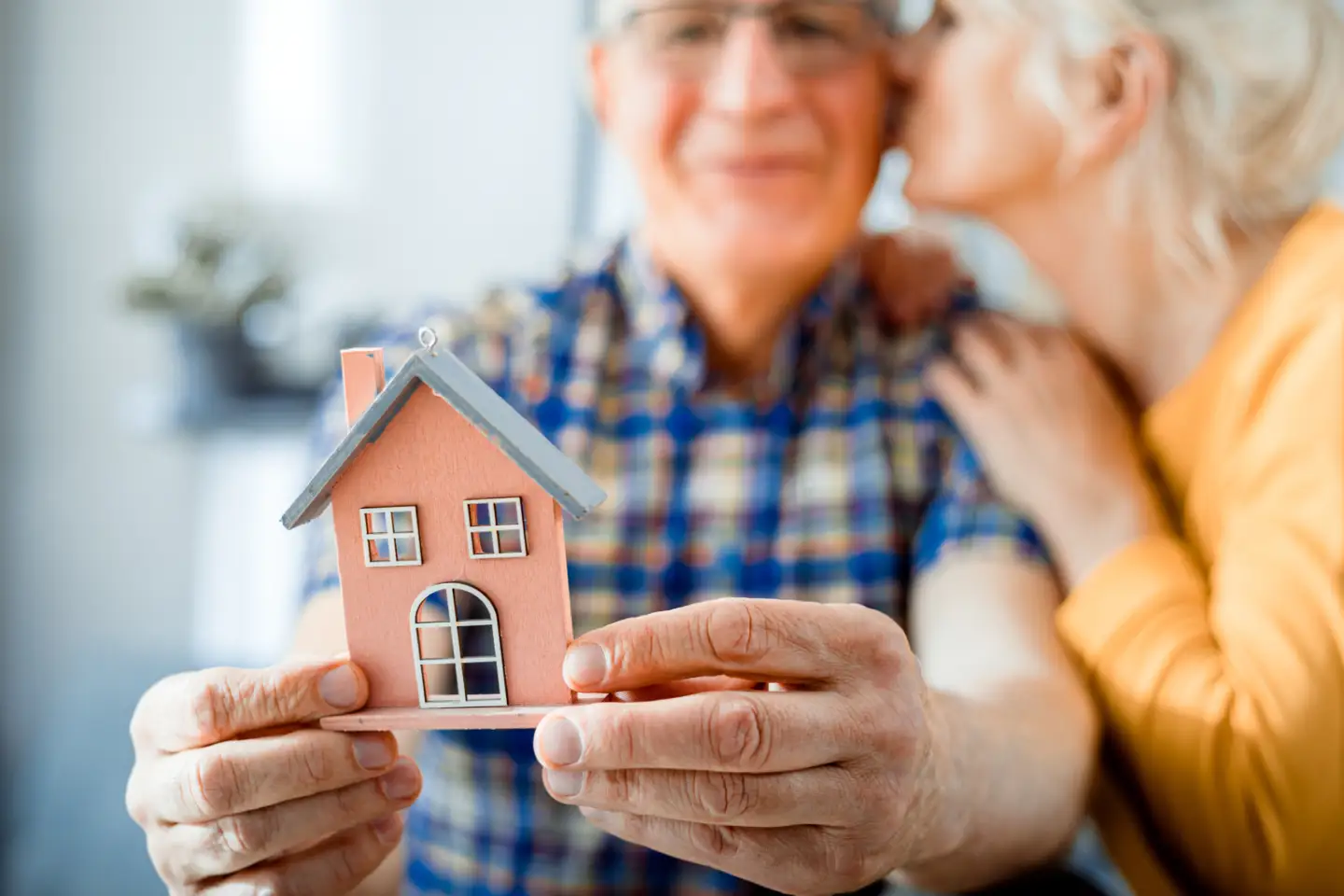 Ein älterer Herr hält ein Modellhaus in der Hand und bekommt einen Kuss auf die Wange