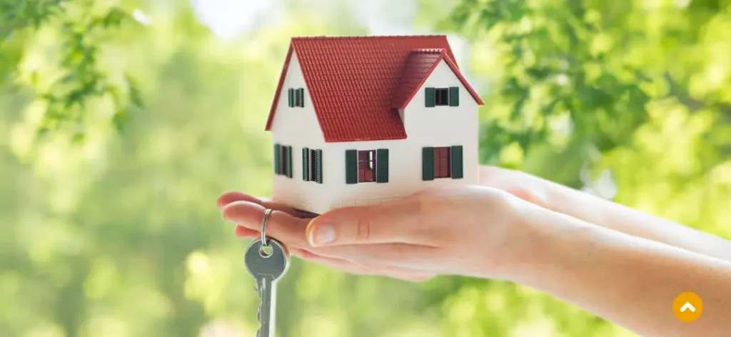Symbolisch Haus kaufen am Niederrhein hält jemand ein Haus in Händen und am Finger hängt ein Schlüssel. 