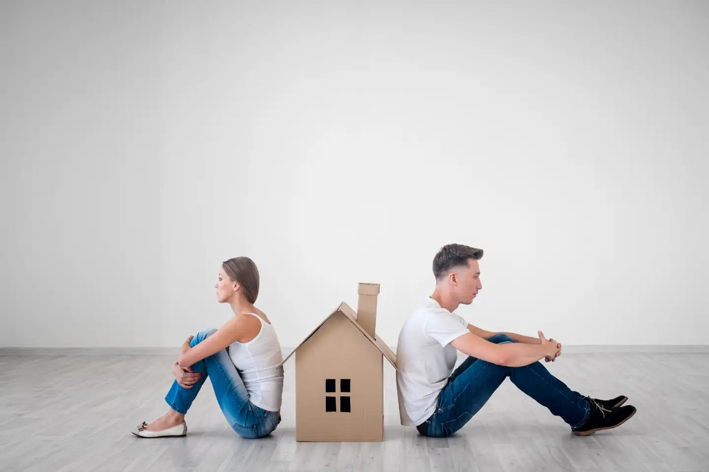 Eine Frau und ein Mann wenden sich sitzend den Rücken zu und zwischen Ihnen steht ein Modellhaus
