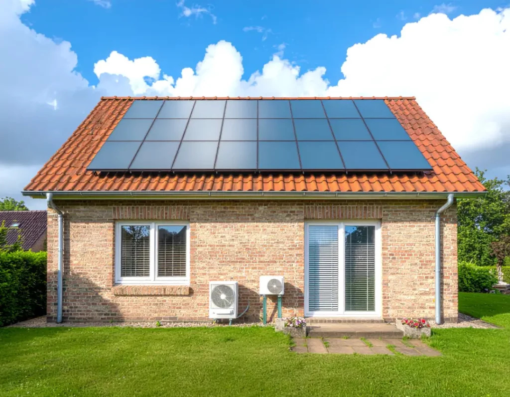 Ein Haus im Grünen hat eine Photovoltaik auf dem Dach und eine Wärmepumpe vor dem Haus. 