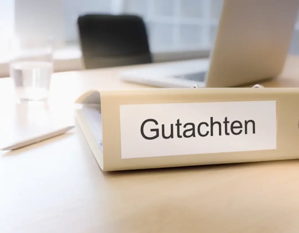 Auf einem Schreibtisch liegt ein Aktenordner, der ein Gutachten beinhaltet. 