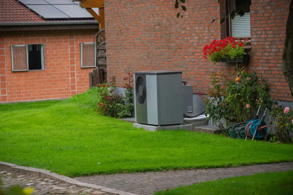 Wärmepumpe steht vor einem Altbau in einem Vorgarten. 
