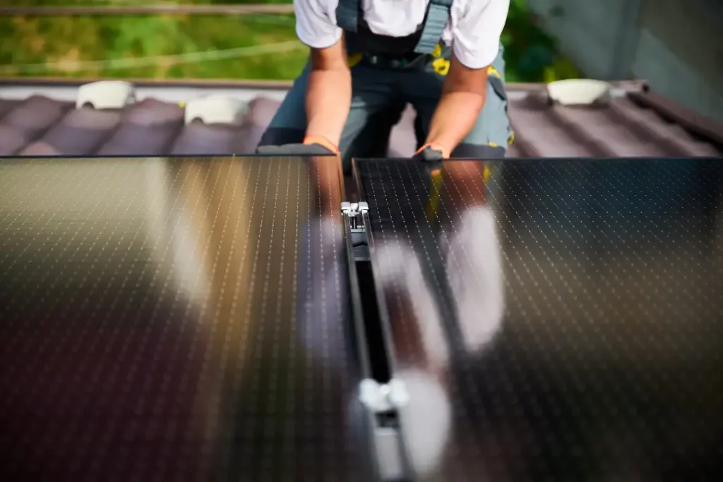 Handwerker spiegelt sich in einer Photovoltaik beim Anbringen auf dem Dach.